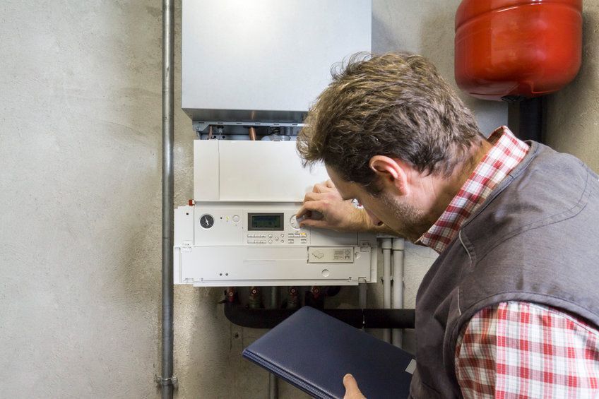 A man is looking at a boiler while holding a notebook.