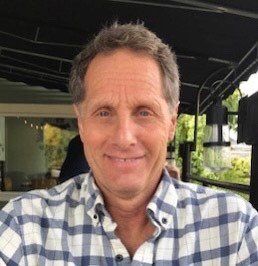 A photo of Board President Ken Schatz looking at the camera wearing a white and grey plaid shirt.