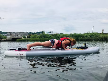 A woman is doing push ups on a paddle board in the water.