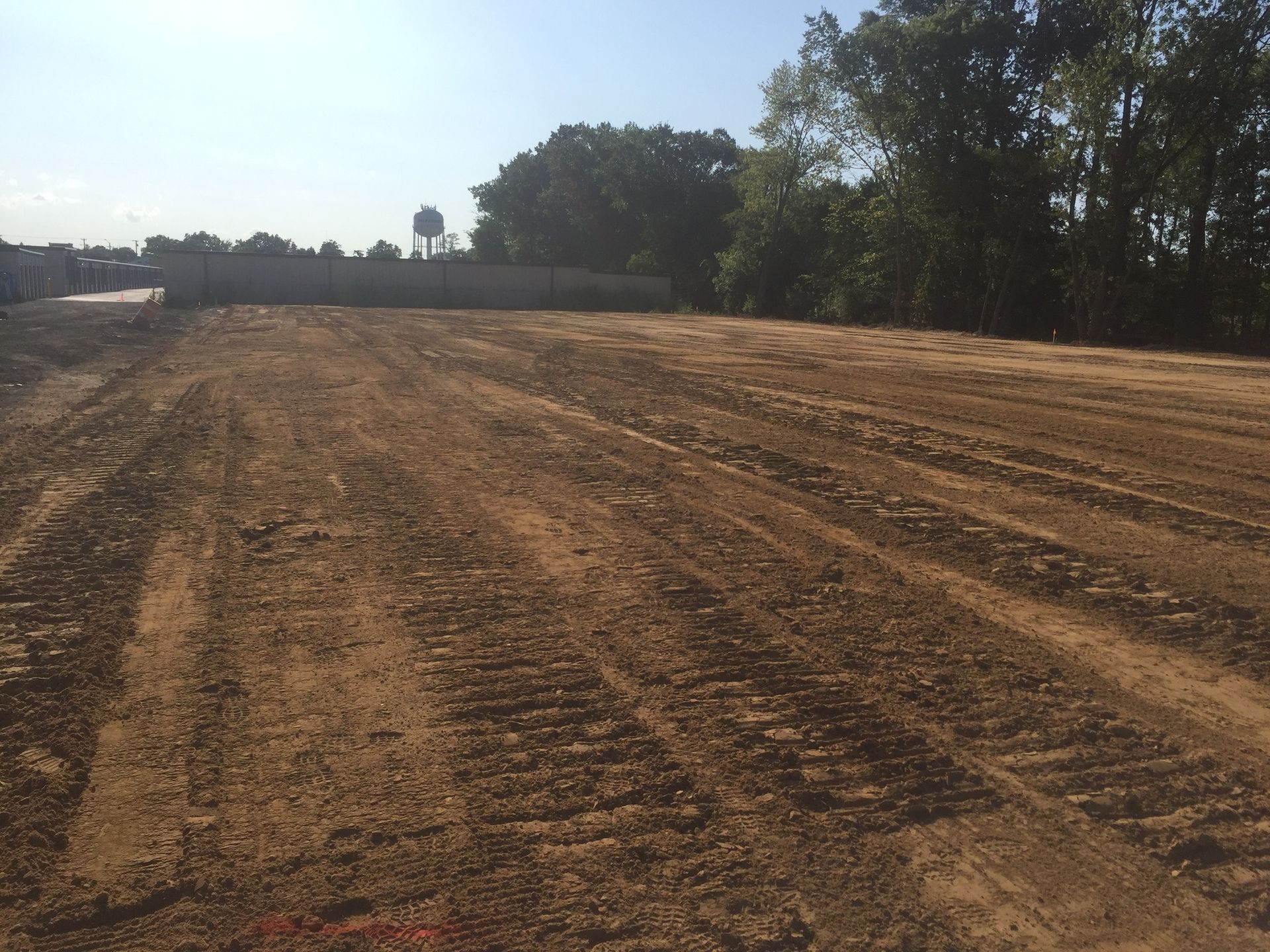 Plowed field of dirt under a blue sky, with trees in the background.