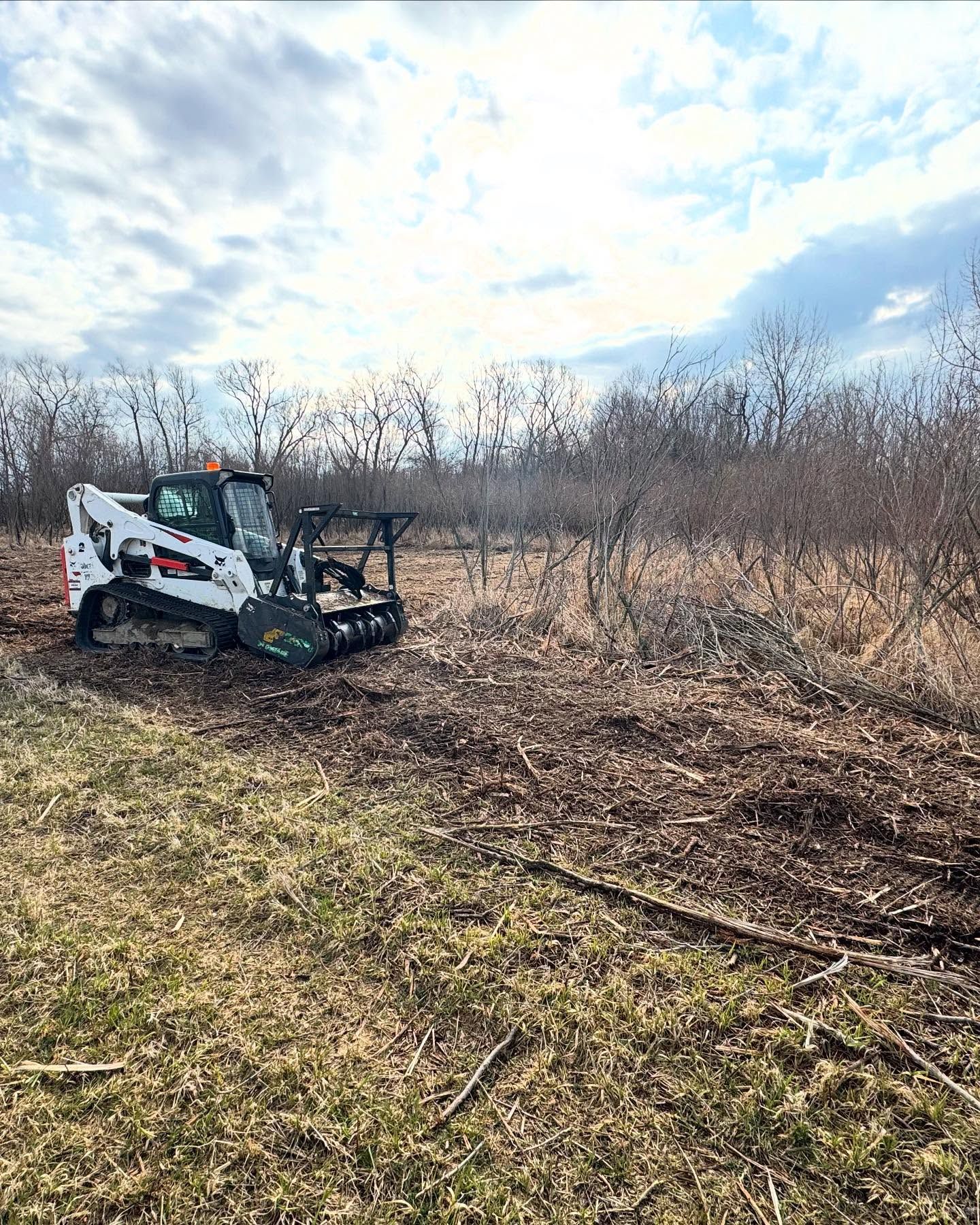 White Bobcat skid-steer mulching vegetation in a field on a cloudy day.