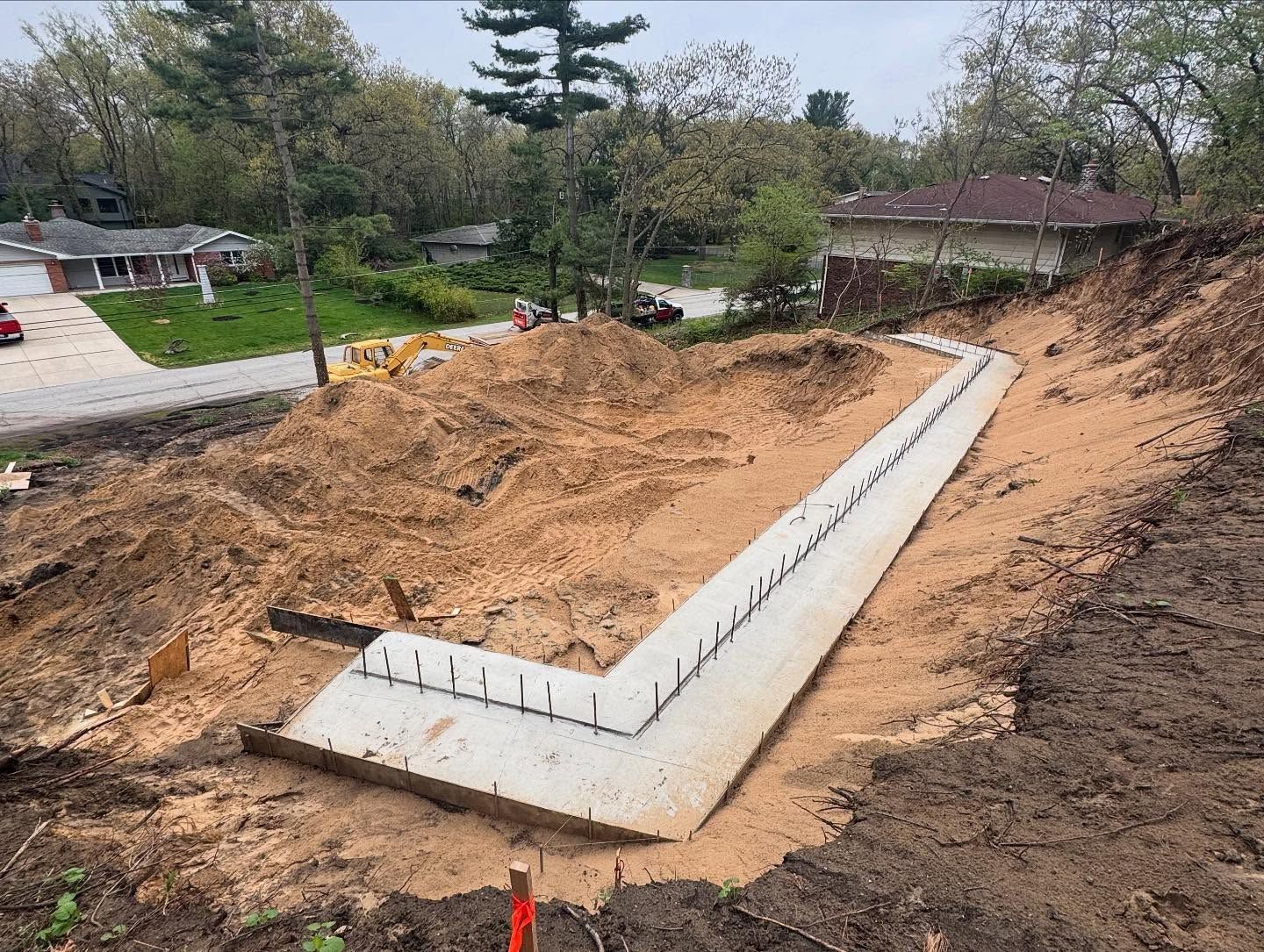 Foundation construction on a sloped lot; L-shaped concrete formwork with rebar, surrounded by dirt and construction site.