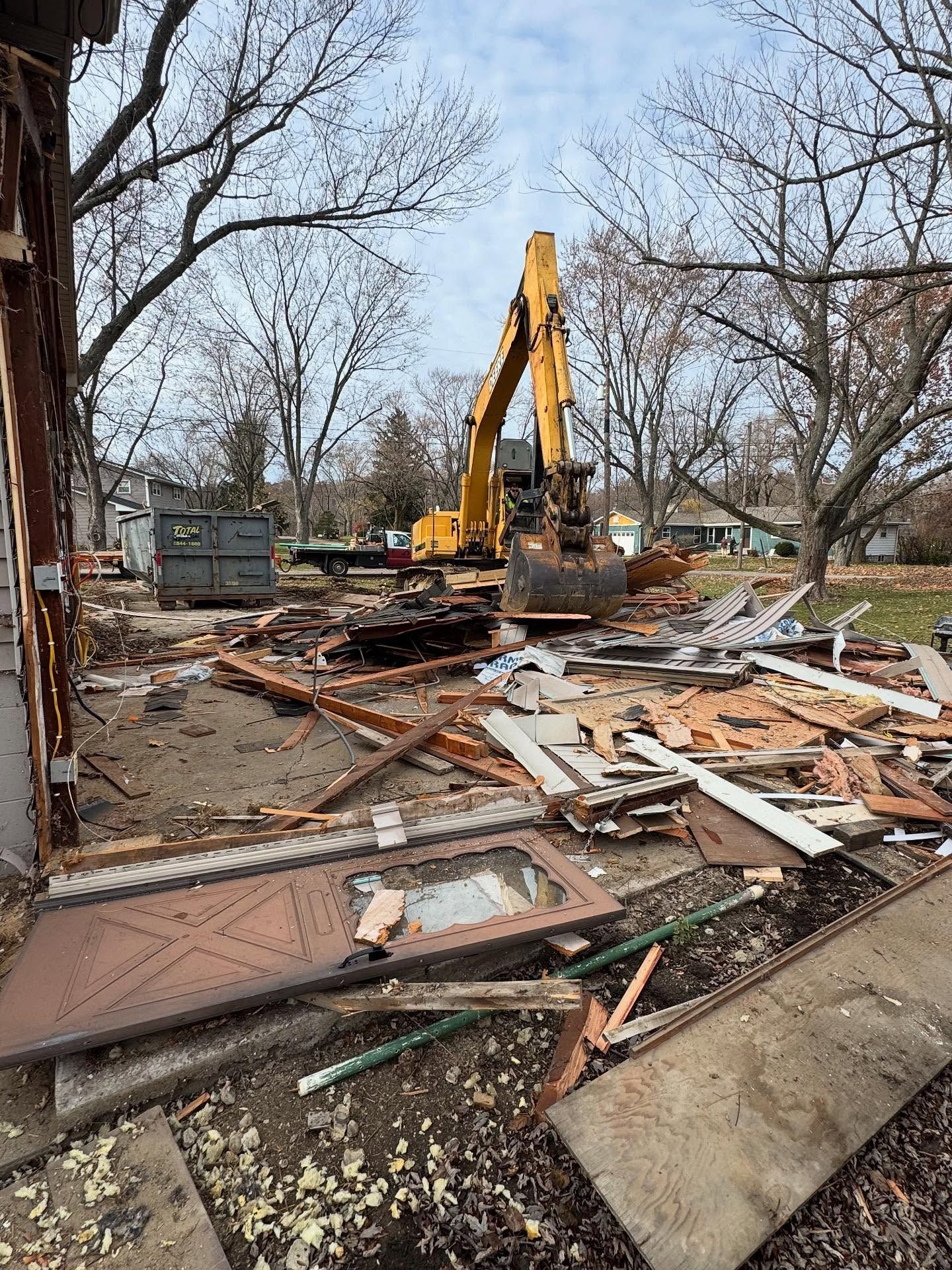 Demolition of a building site with an excavator in action; debris and a dumpster. Overcast sky.