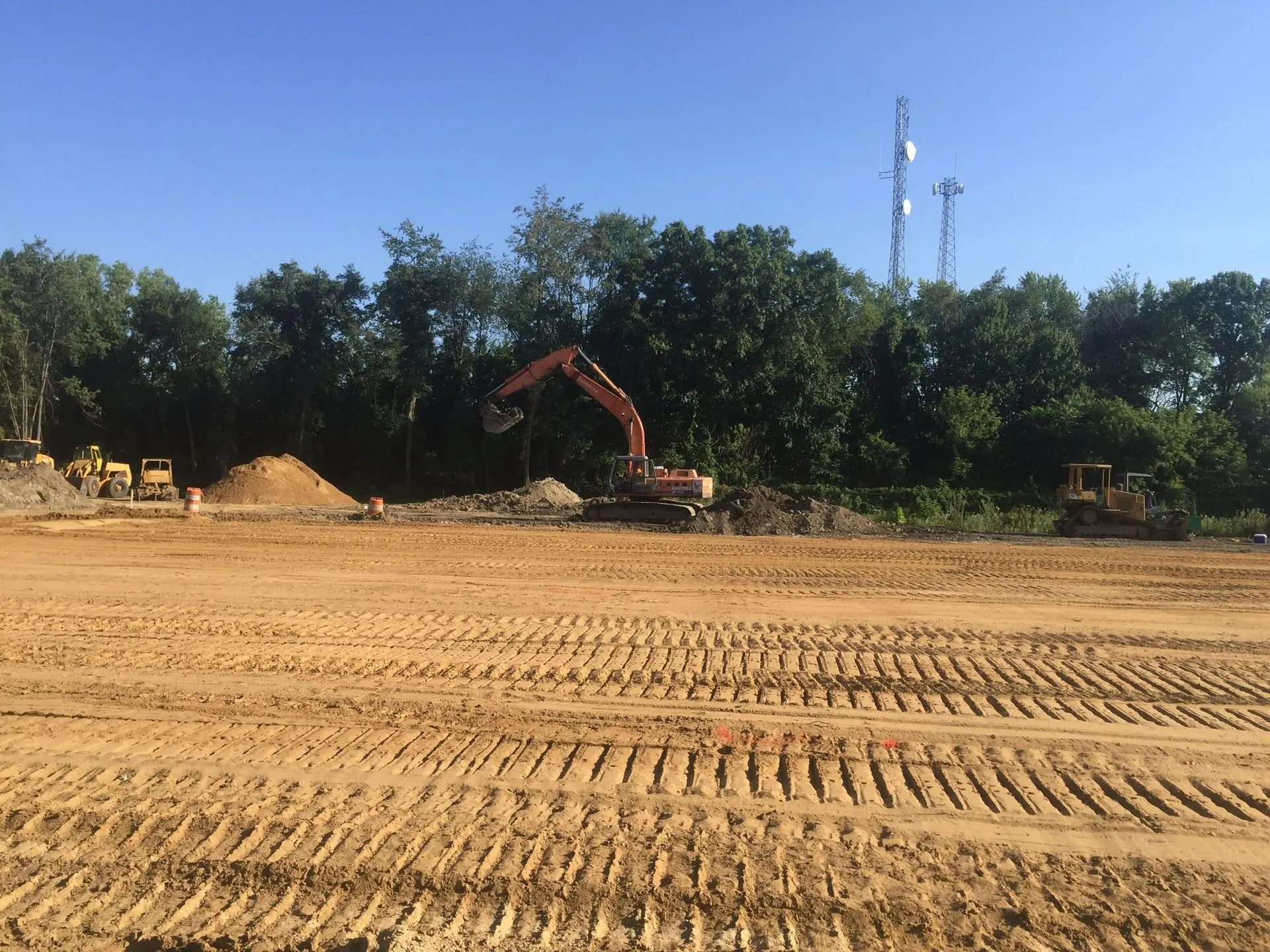 Construction site with heavy machinery like an excavator, trees, and blue sky.