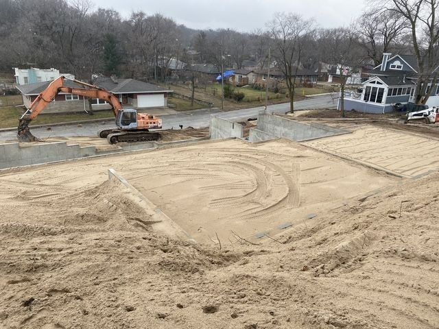 Construction site with excavator and sand. Residential neighborhood in the background.