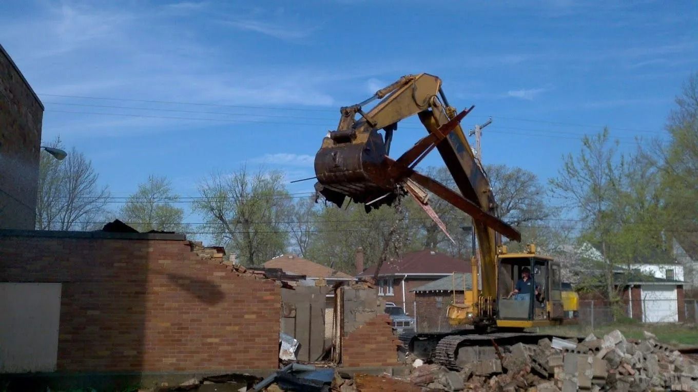 Yellow excavator demolishing a brick building under a clear blue sky.