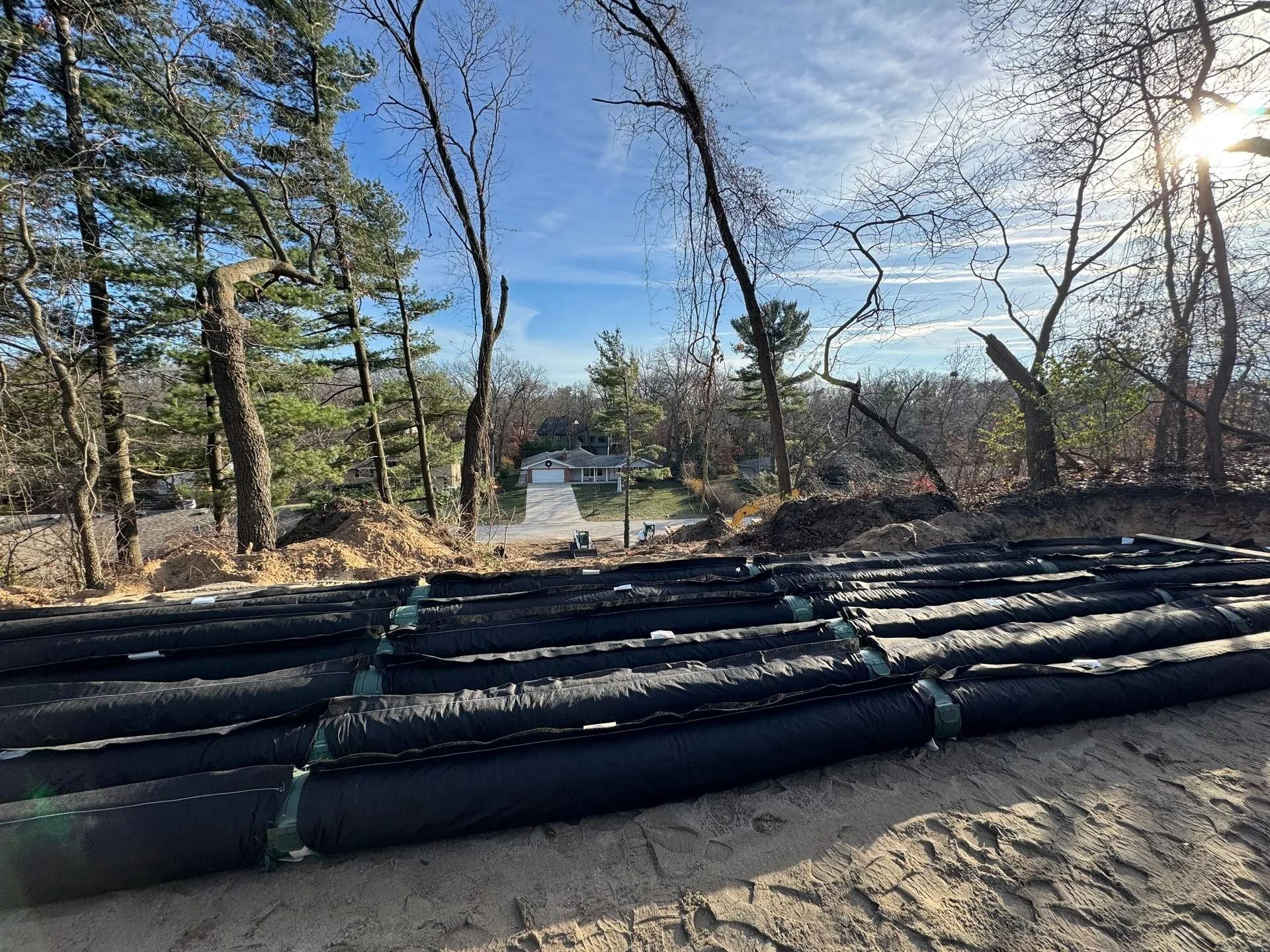 Black rolled landscape fabric on a sandy hillside, overlooking a path and trees under a blue sky.