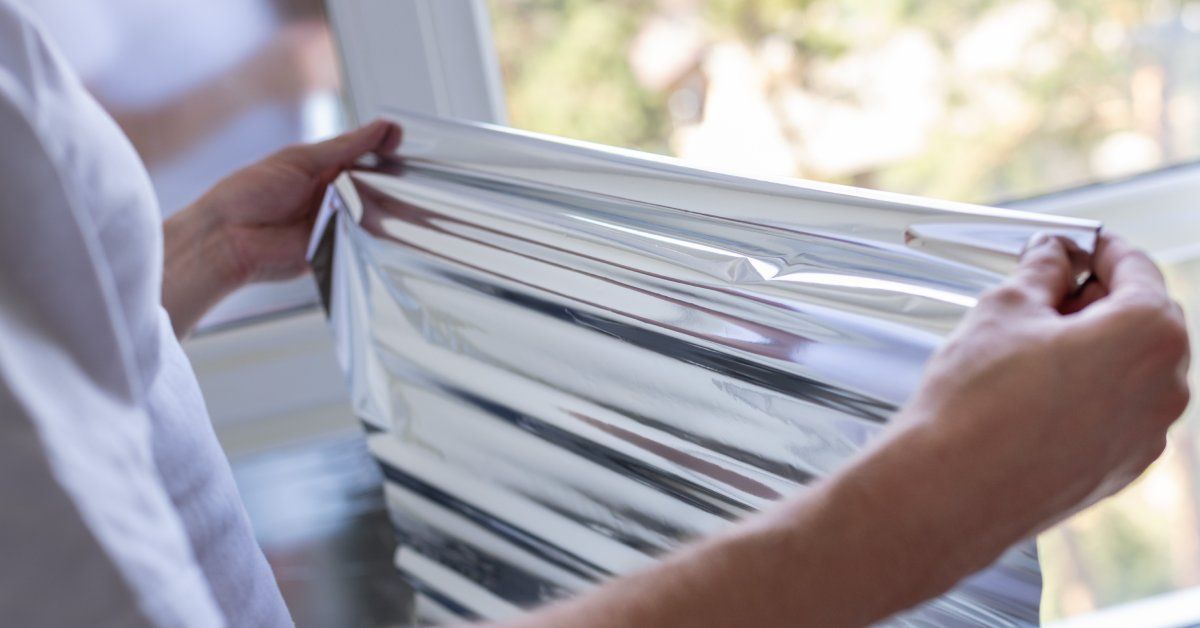 A close-up shot of a man's hands stretching out a piece of window film up to a window for tinting.