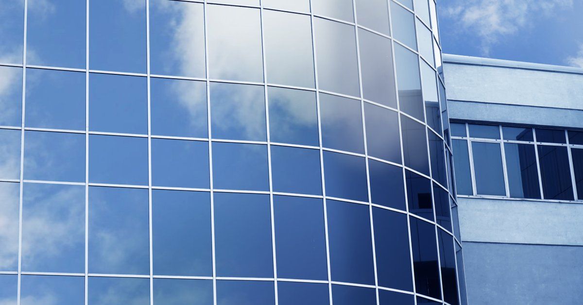 A modern, glass skyscraper with all of the windows tinted, reflecting the blue sky.