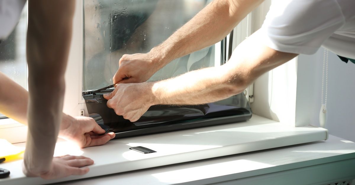 Two workers applying window film, using a blade to cut off the excess film at the bottom of the wind