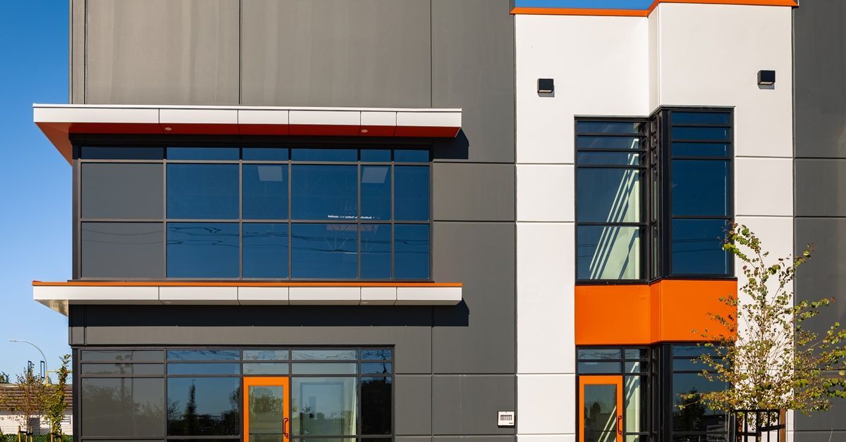 A modern building with black and white walls and orange accents. The windows are dark so people cannot see inside.