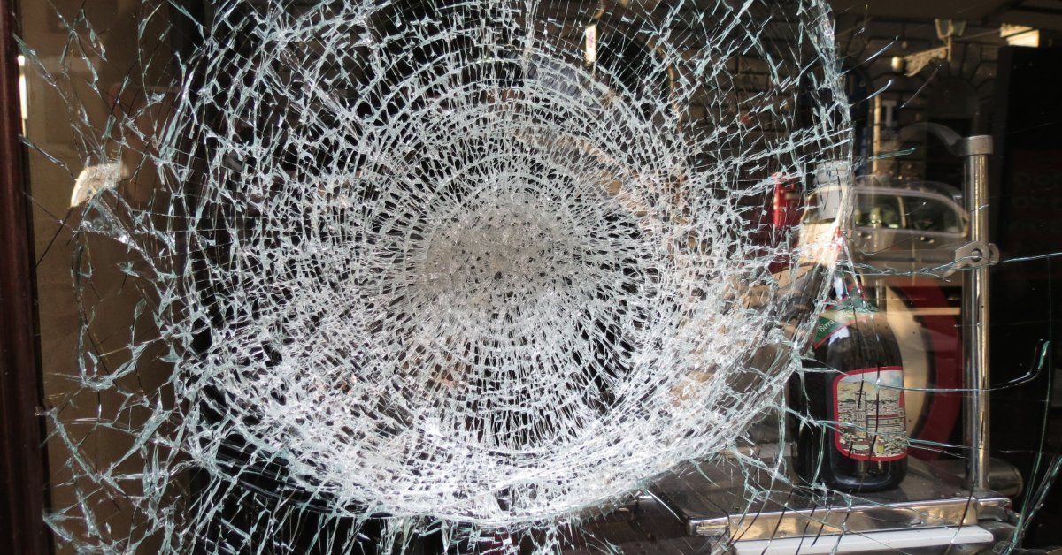 A front shop window with a large dent smashed into it; the fracture is a large, spiderweb structure.