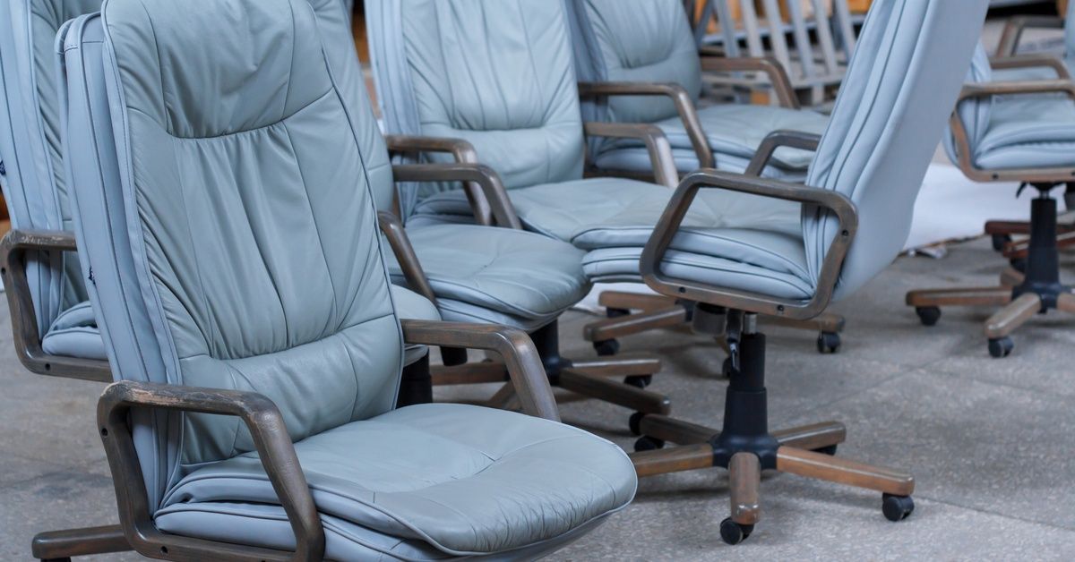 Eight gray leather office chairs sit on large gray tiles, each showing visible signs of wear and fading.