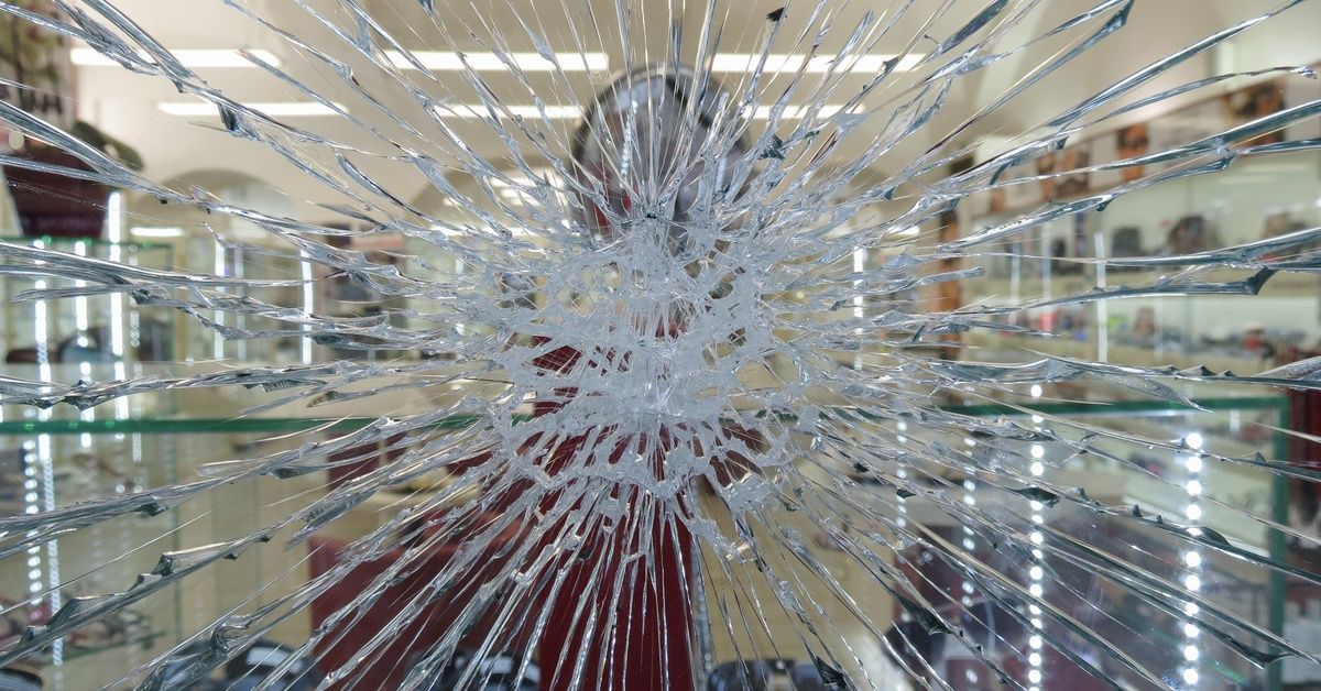 A store window has a centralized impact with shattered glass, but the glass remains intact without falling or leaving a hole.