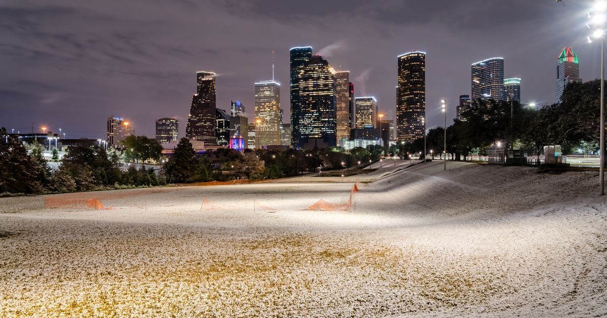 The cityscape of Houston’s tall buildings glows on a winter night, with snow covering the grass in Eleanor Park.