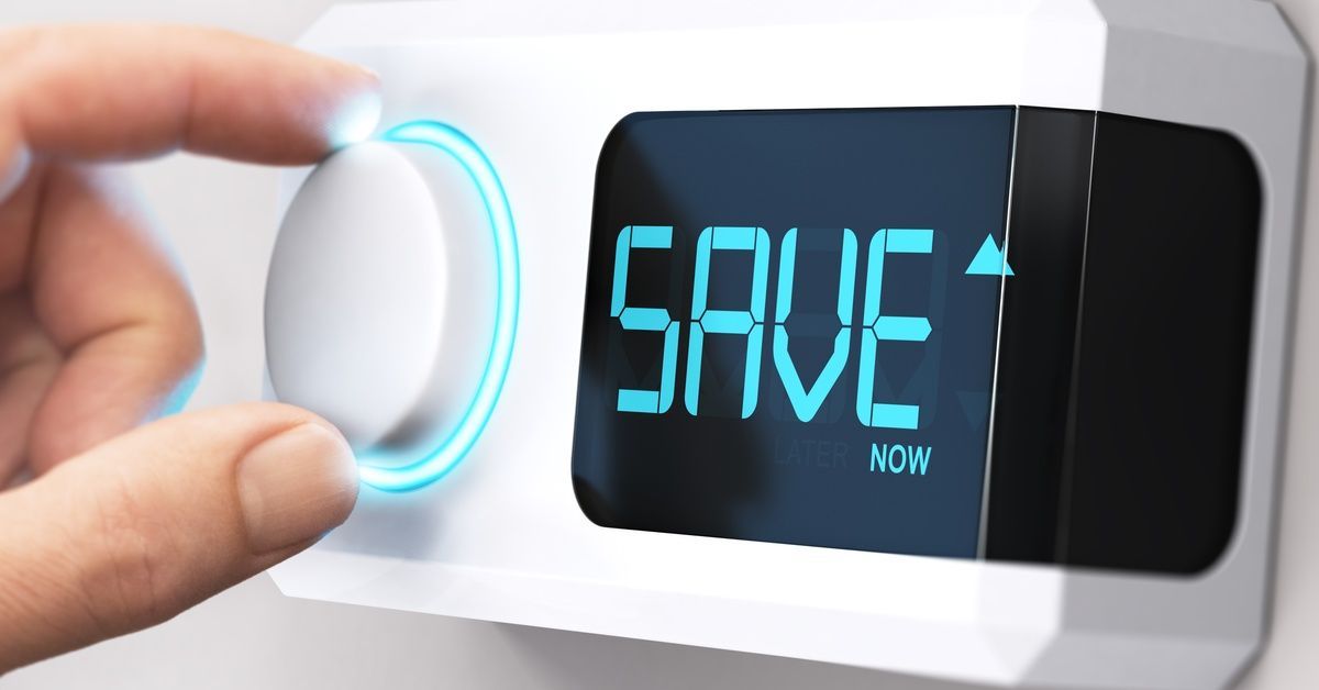 A person’s hand adjusts a turn dial on a white thermostat, with the digital screen displaying “SAVE now” in blue letters.