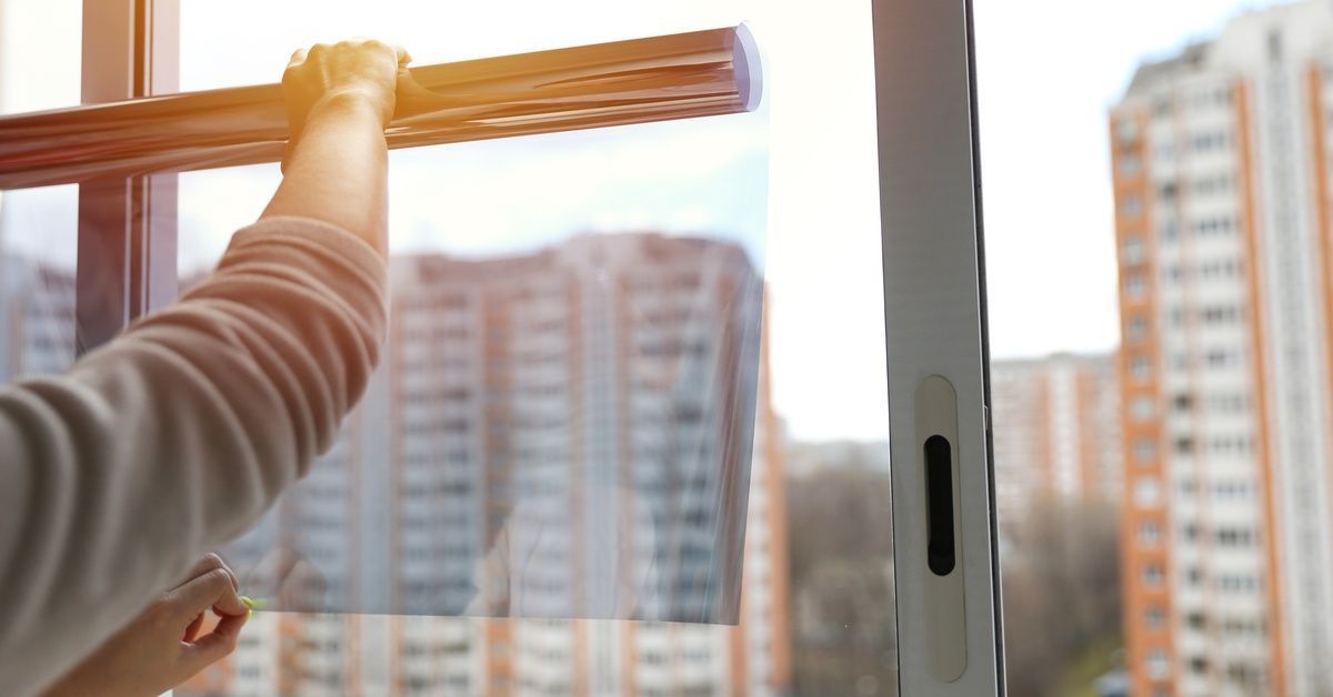 A man holds window film tint against a large window in a tall building as sunlight shines through.