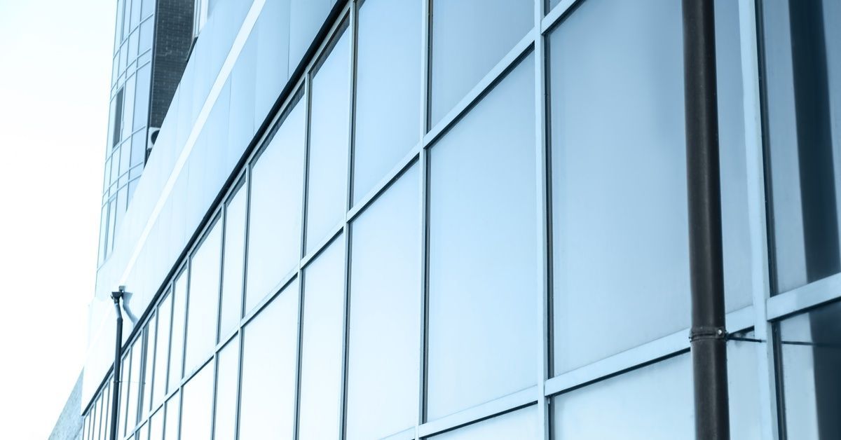 The exterior of a modern multi-level building features large reflective windows that mirror the surr