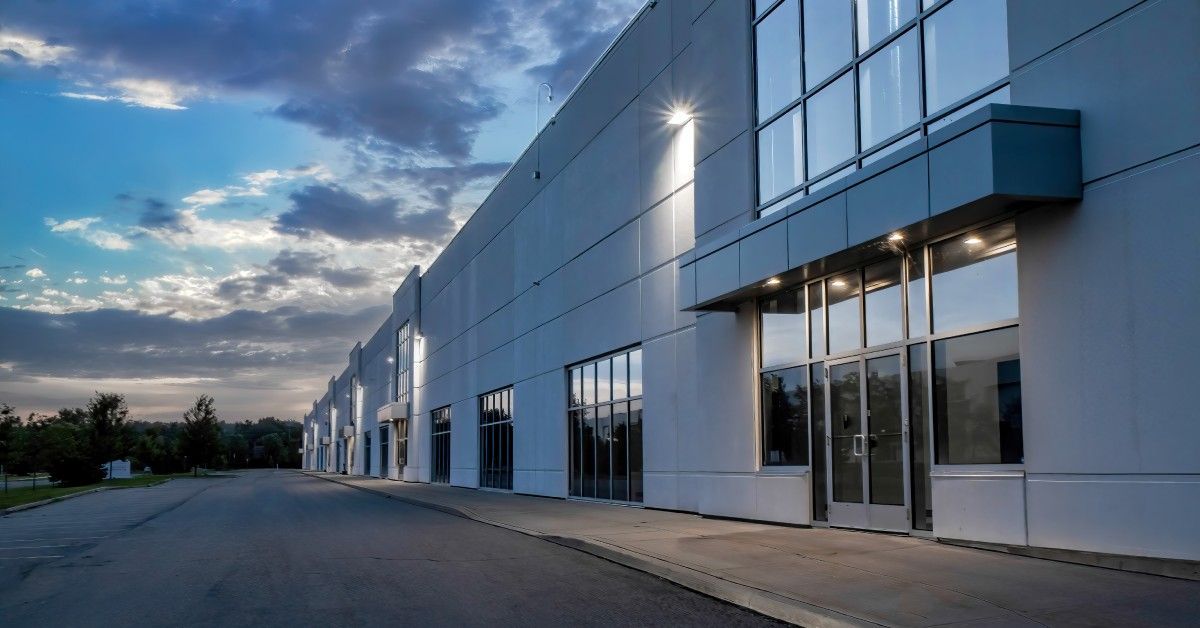 As dusk falls, lights illuminate a business building with a flat facade, highlighting entrances and exterior lighting.