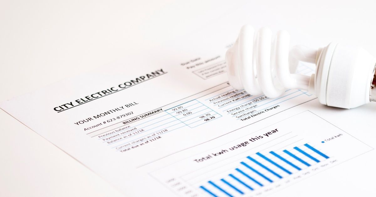 A monthly electric bill from a utility company lies beside a compact fluorescent light bulb.