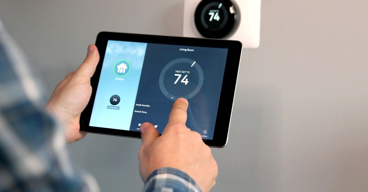 Person adjusting smart home AC/Heating using tablet app while wall-mounted thermostat displays temperature setting.