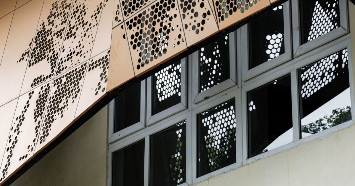 A building exterior features perforated metal panels with circular patterns above a row of glass windows.