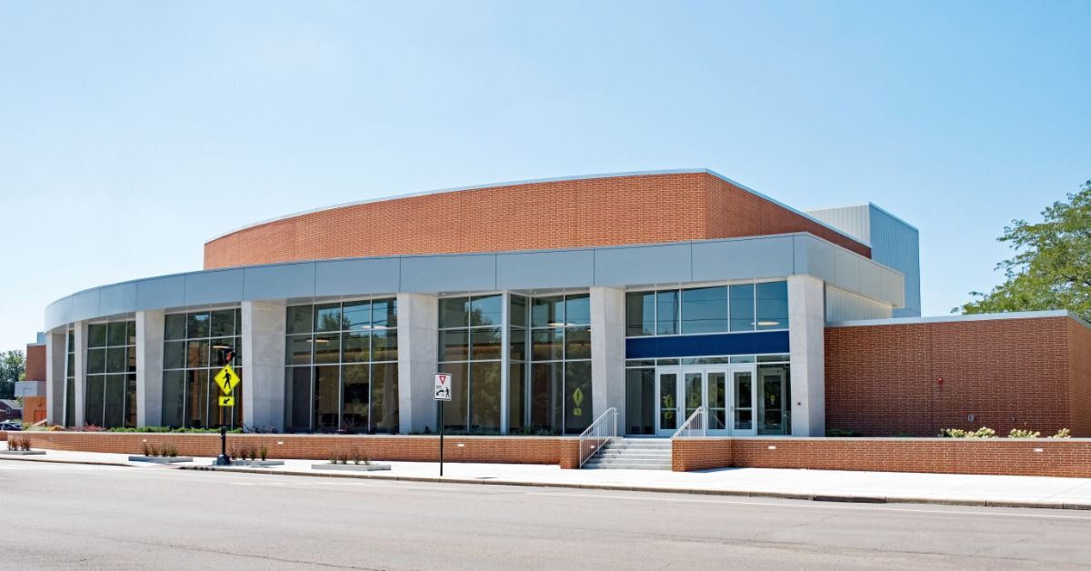 A modern brick building with large glass windows sits along a street, featuring a curved facade.