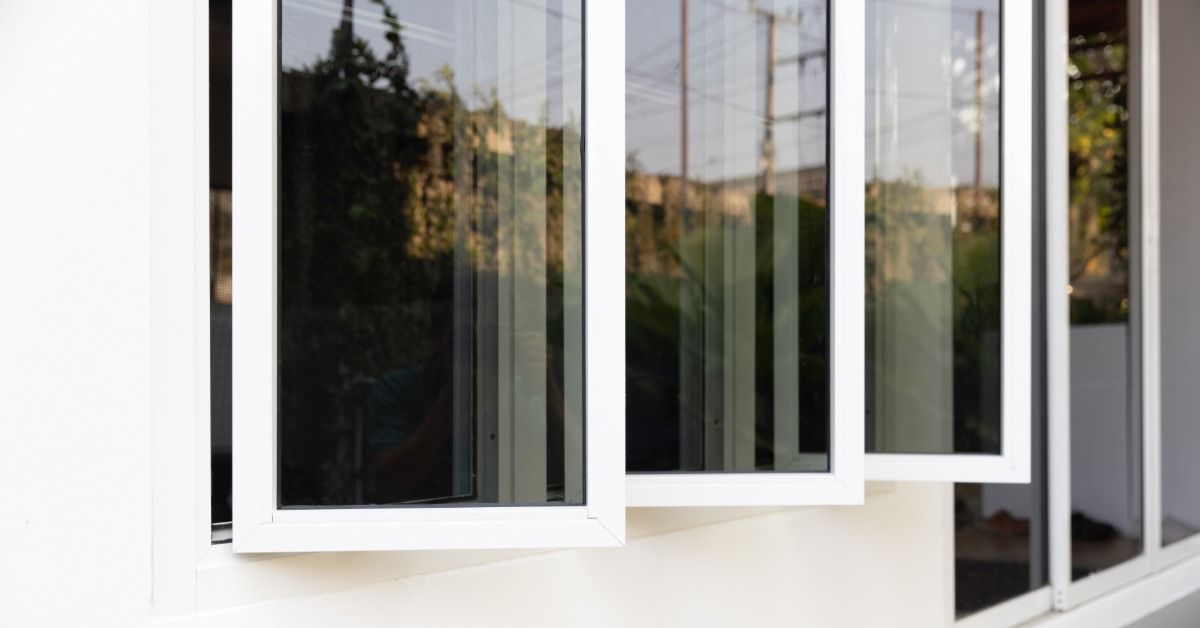 A home's exterior with three oblong windows all open. The windows have window tint on them for privacy.