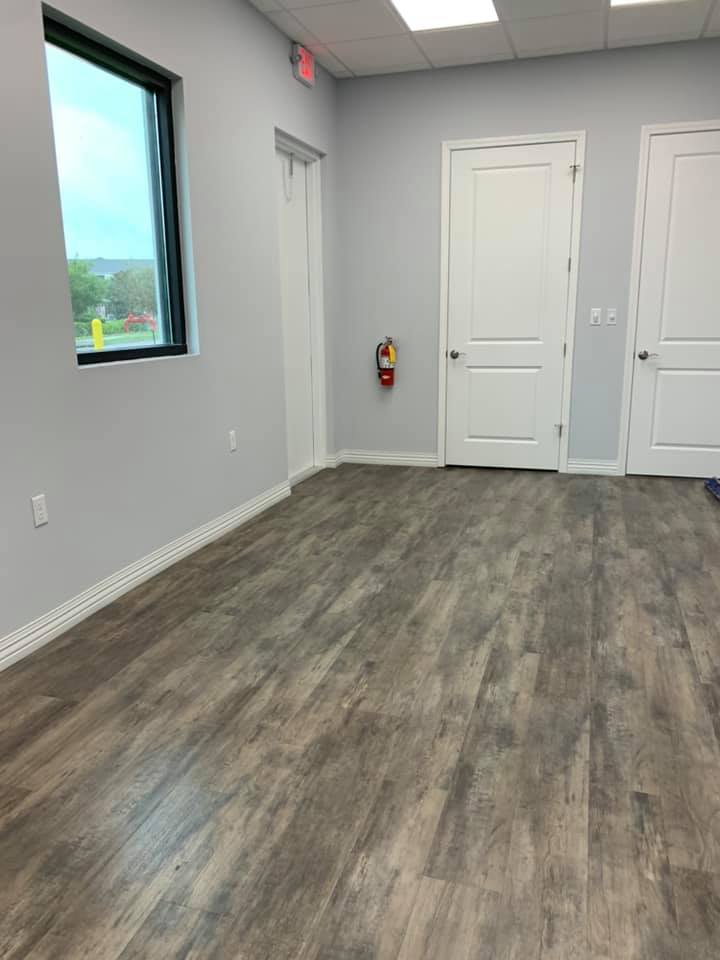 Empty room with gray walls, wood-look floor, window, and white doors. Fire extinguisher on wall.