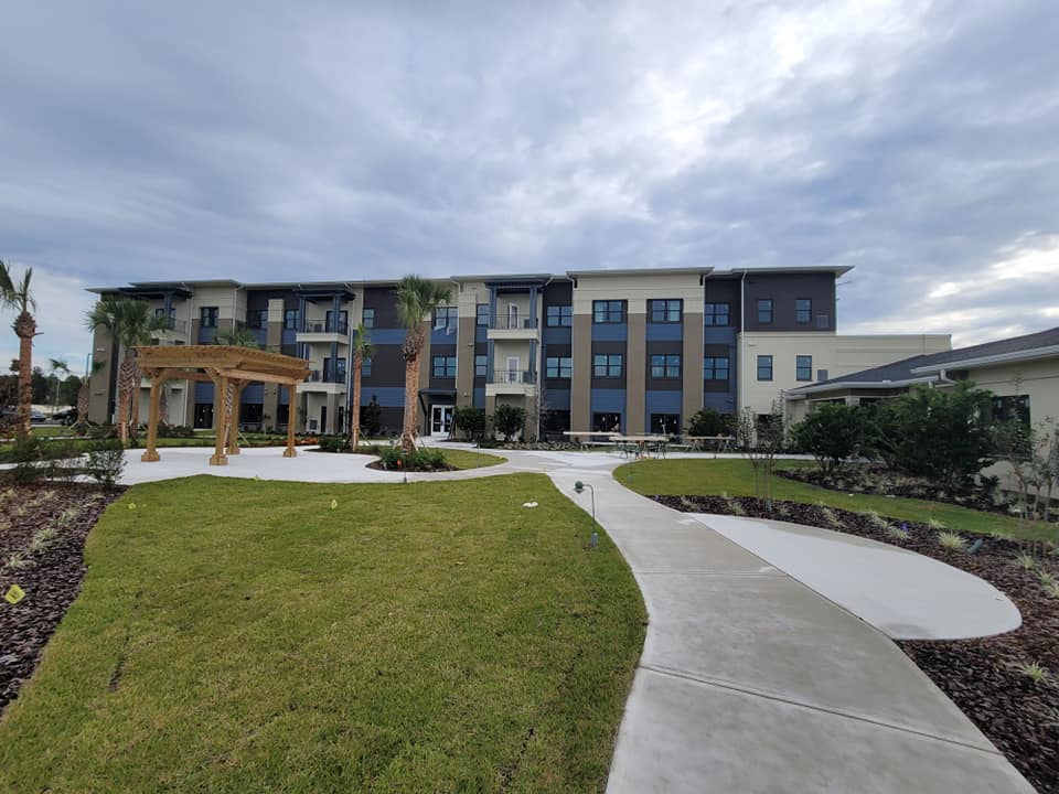 Exterior view of a modern apartment building with a curved sidewalk and grassy lawn under a cloudy sky.