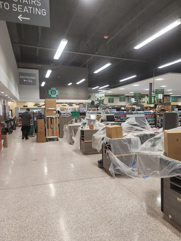 Grocery store interior with construction: cash registers covered, boxes, shopper with cart, signs.