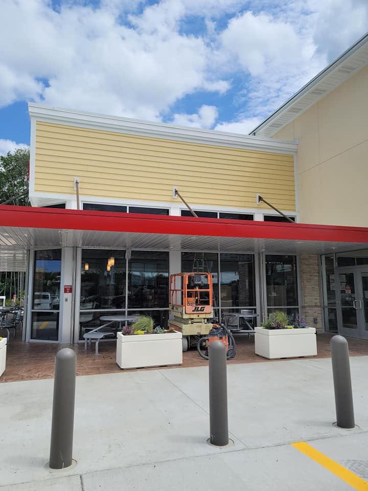 Exterior of a restaurant with red awning, yellow siding, and large windows. A lift is visible near the entrance.