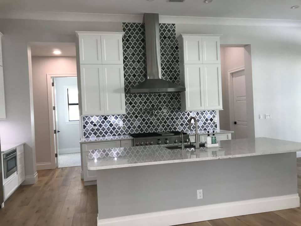 Modern kitchen with white cabinets, grey island, and a patterned backsplash.