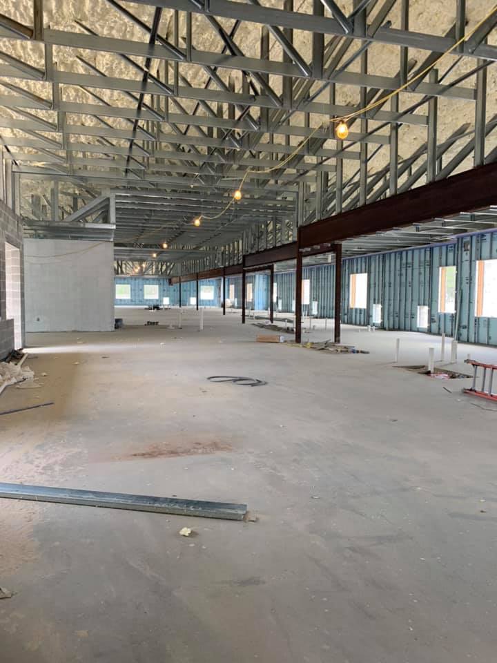 Interior of a building under construction: steel framing, concrete floor, windows, and open space.