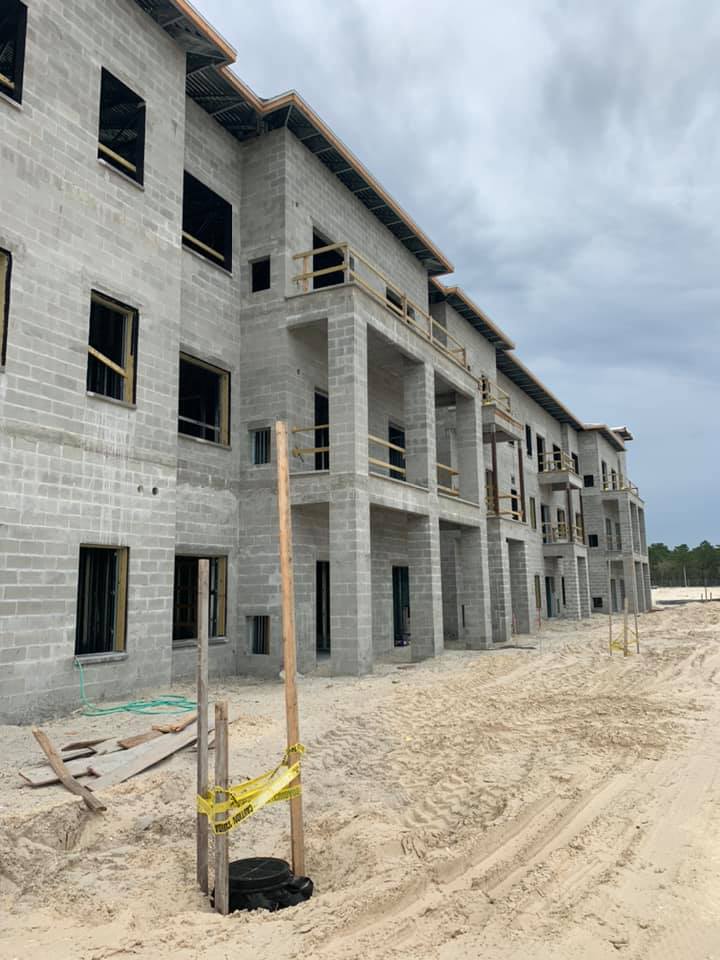 Construction site of a multi-story concrete building. Sand surrounds the structure, under a cloudy sky.