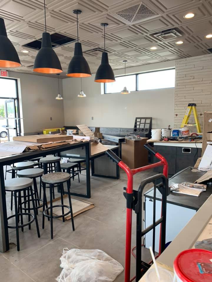 Interior construction scene: restaurant with tables, stools, ceiling lights, and unfinished details.