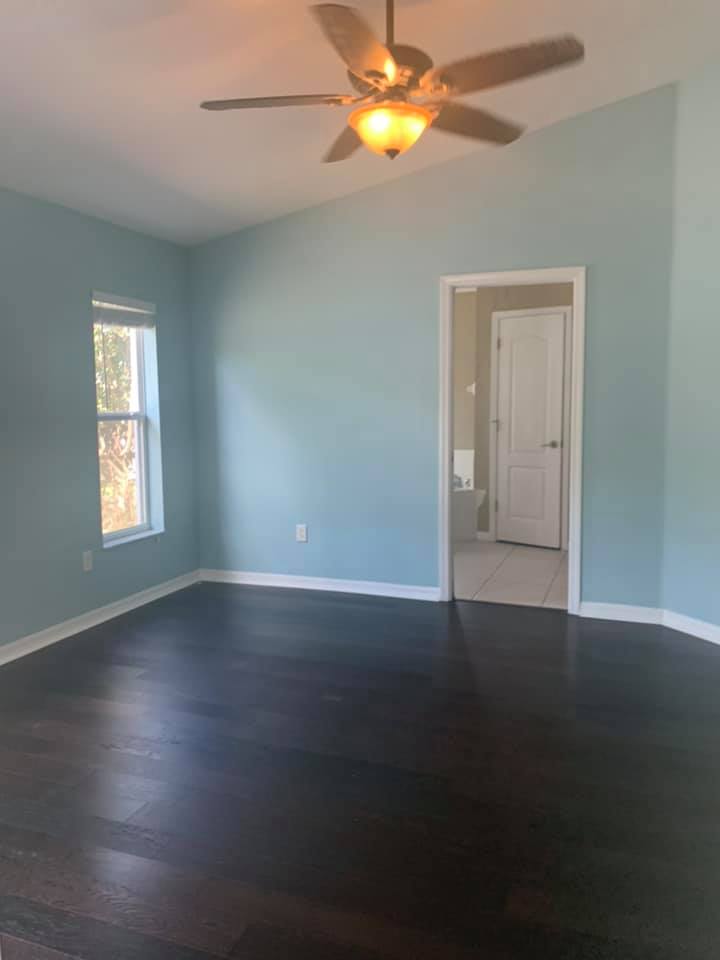 Empty bedroom with dark wood floor, light blue walls, white trim, and a ceiling fan.
