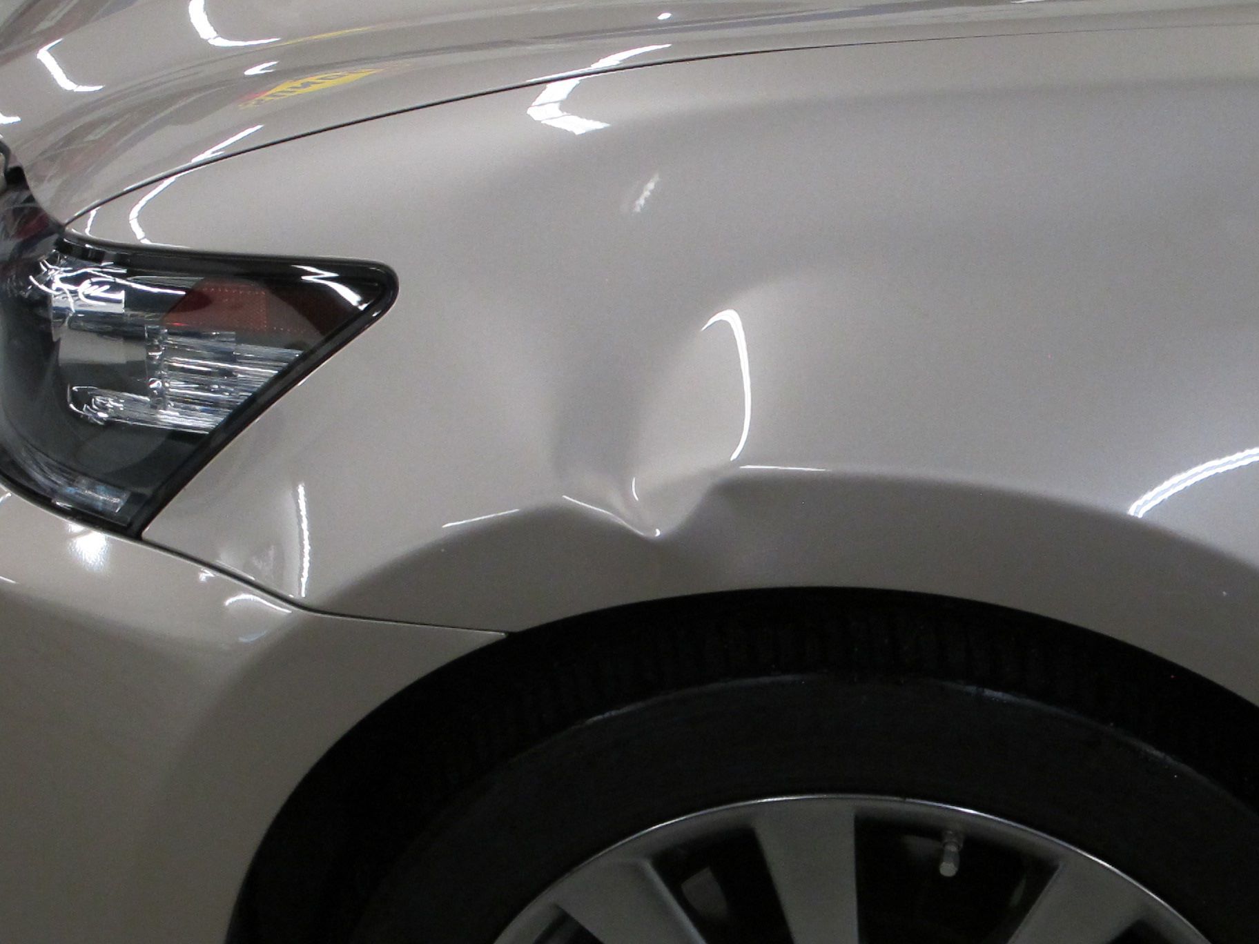 A close up of a white car with a damaged fender