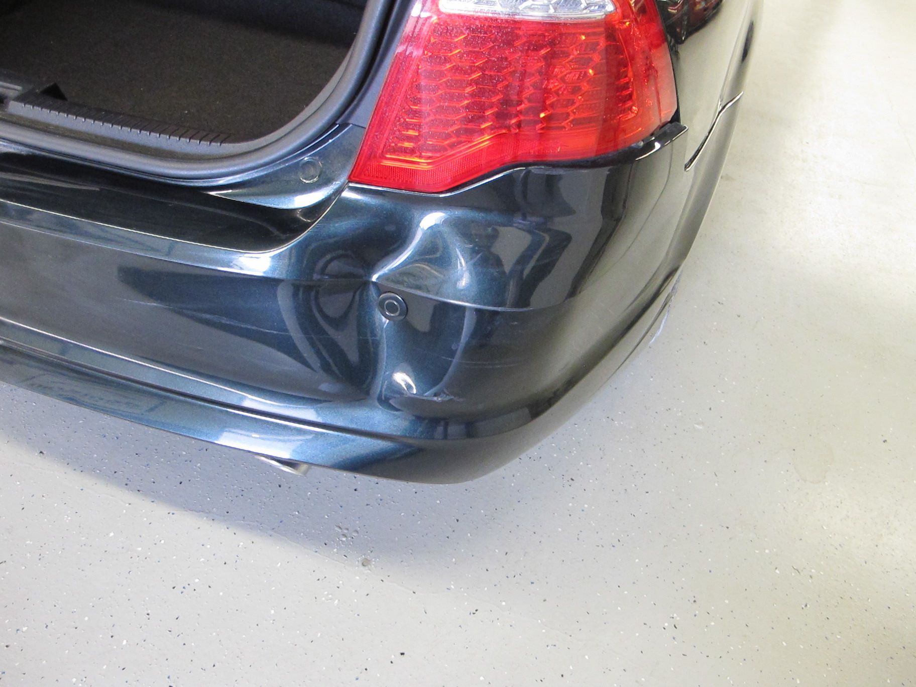 A black car with a damaged bumper is parked in a garage