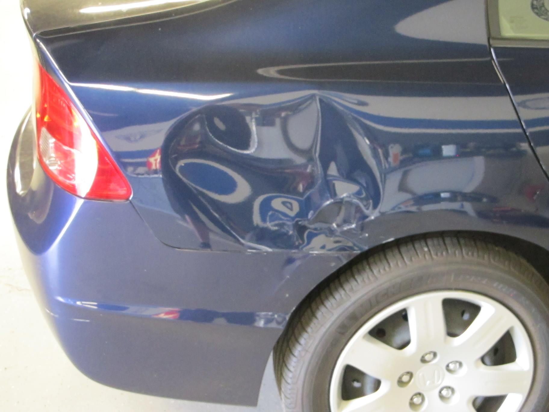 A blue car with a damaged fender is parked in a garage