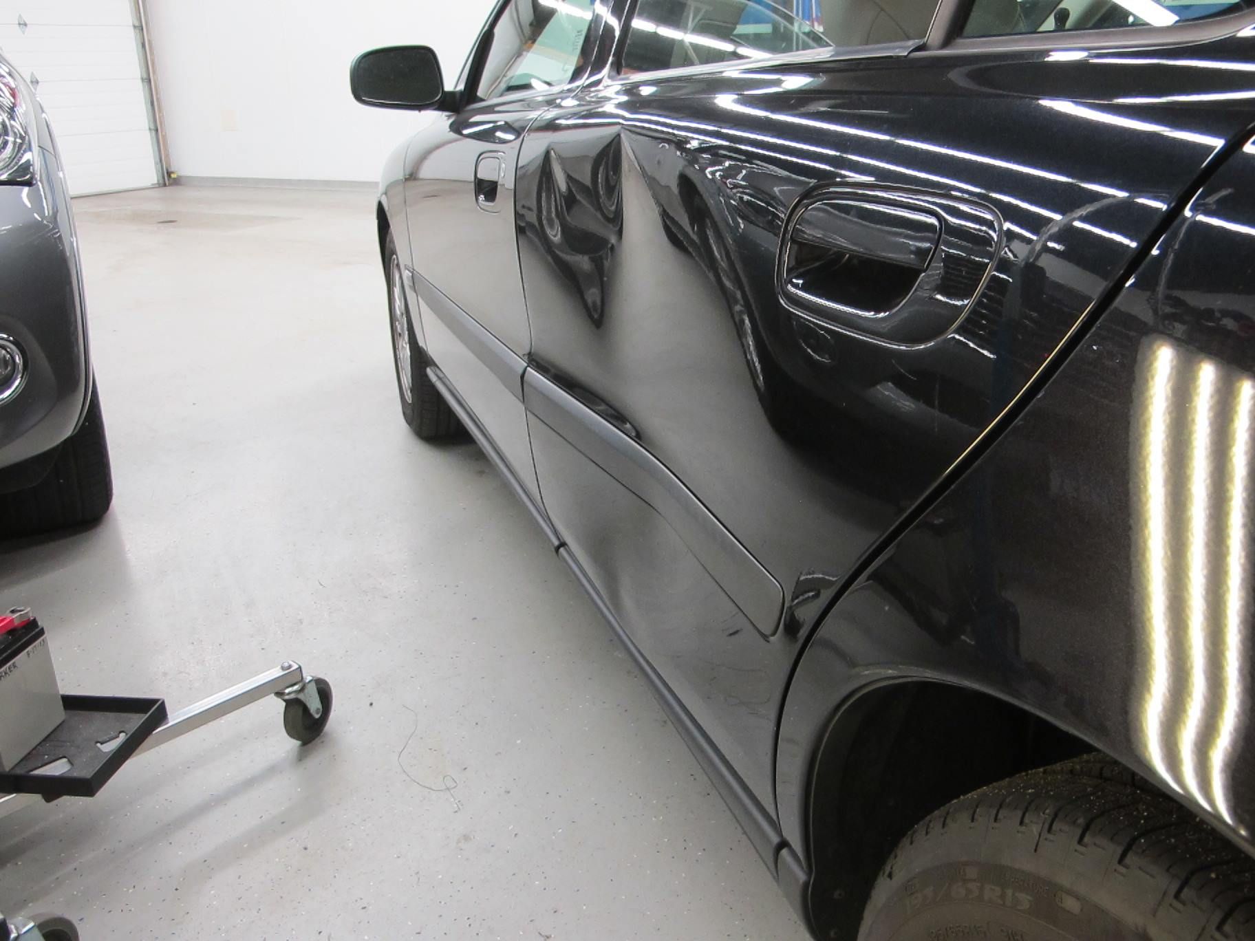 A black car is parked in a garage next to another car