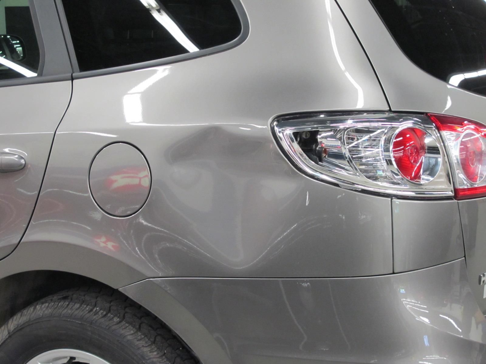 A silver car with a damaged fender is parked in a garage