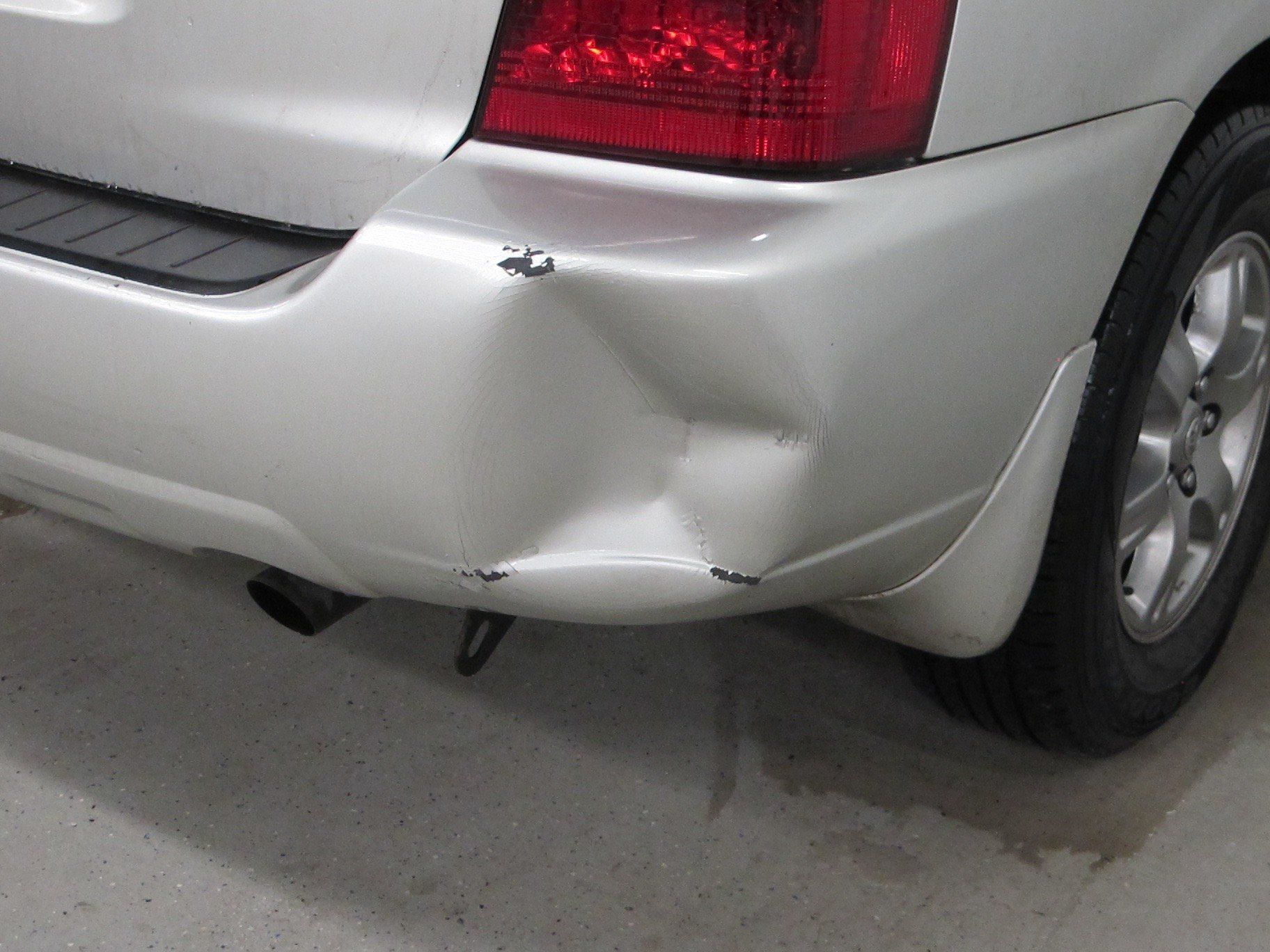 A silver car with a damaged bumper and tail light