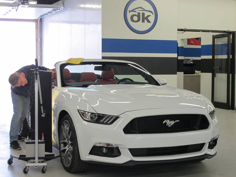 A man is working on a white mustang convertible in a garage.