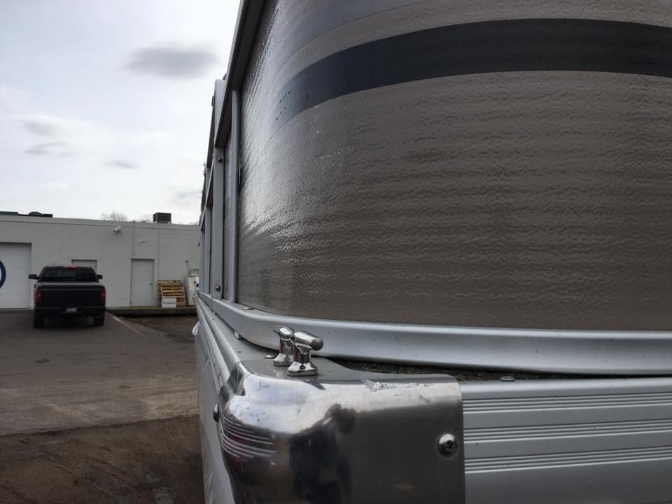 A pontoon boat is parked in a parking lot next to a truck.