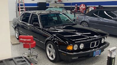 A black bmw is parked in a garage next to a red stool.