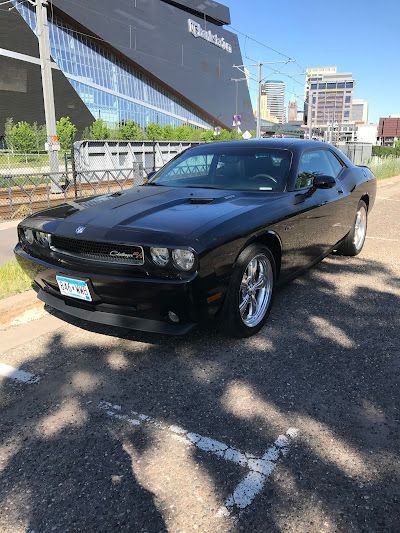 A black dodge challenger is parked in a parking lot in front of a building.