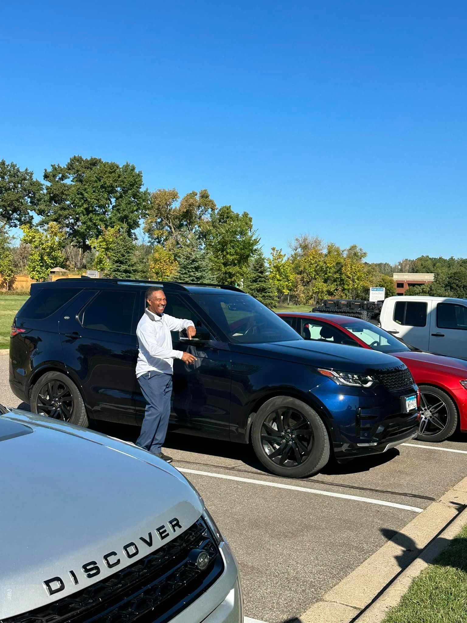 A man is standing next to a blue land rover discovery in a parking lot.