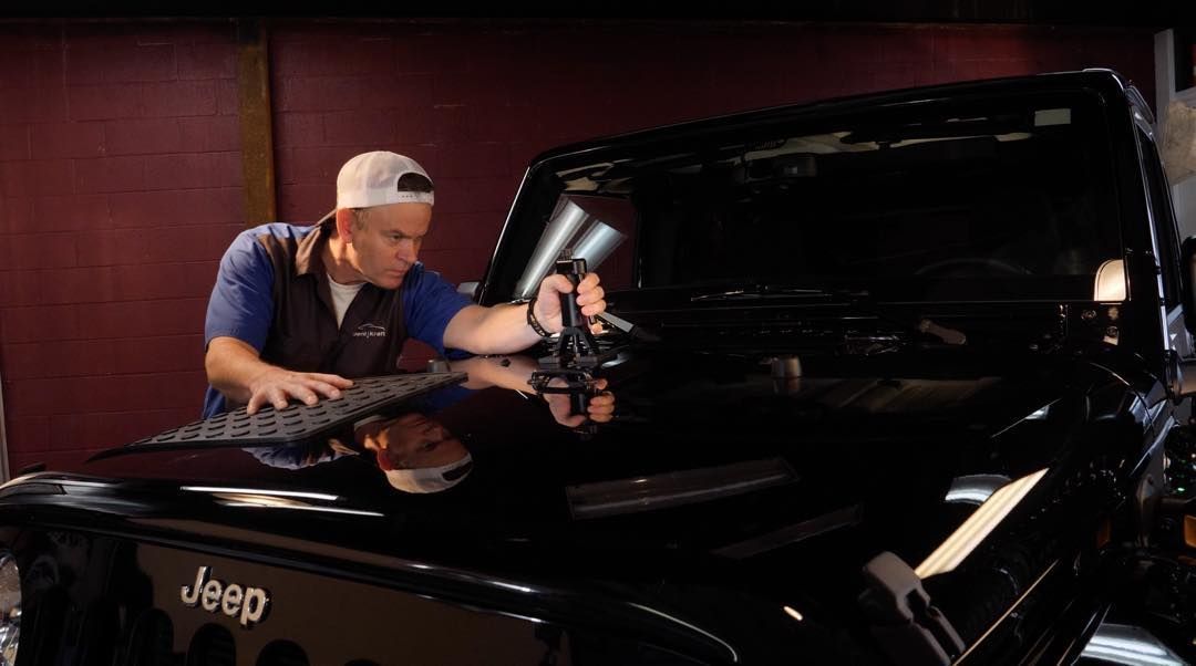 A man is working on the hood of a black jeep.