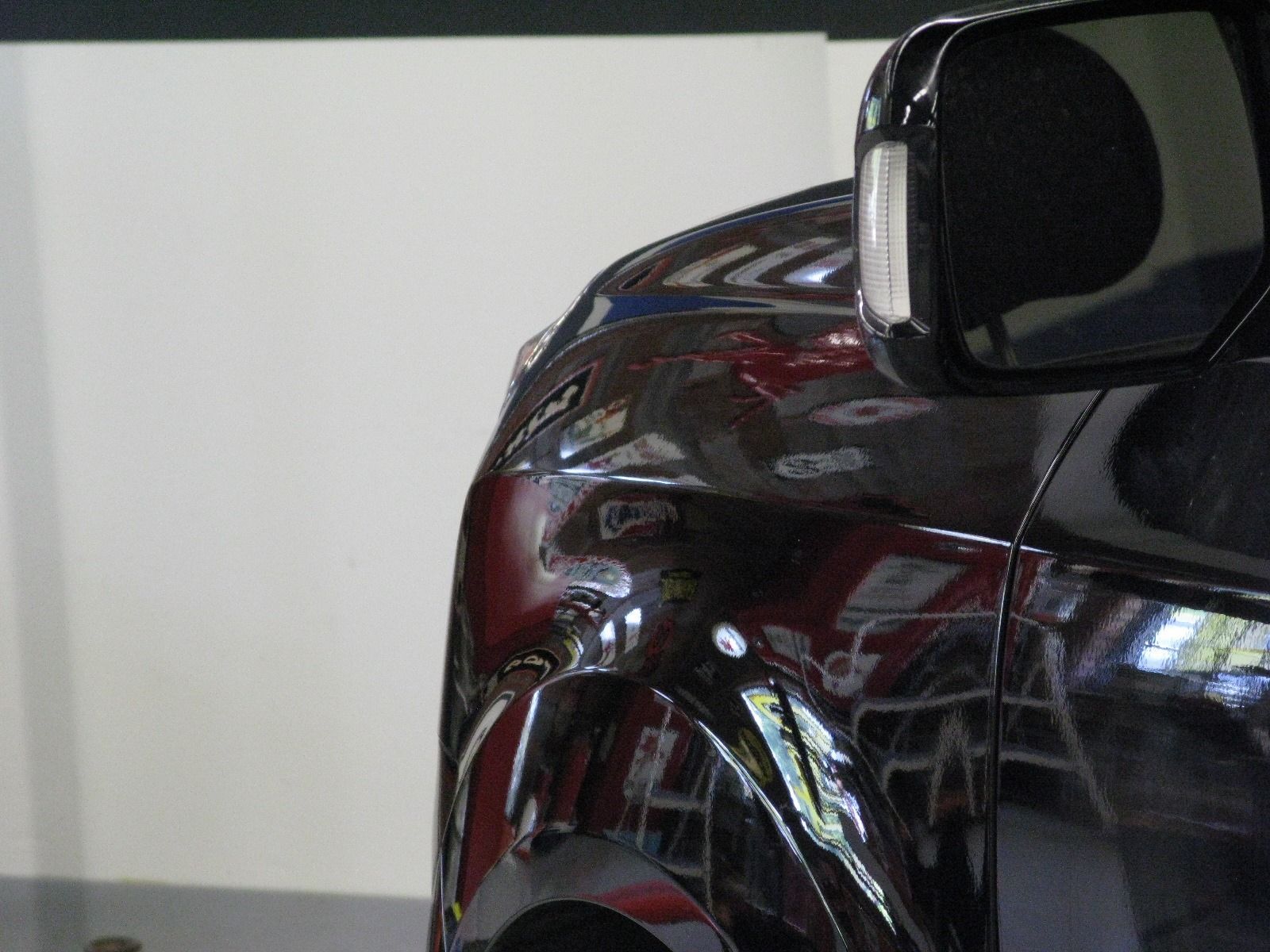 A black car is parked in front of a white wall